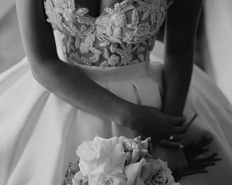 Black and white image of a person wearing a lace wedding dress holding flowers.