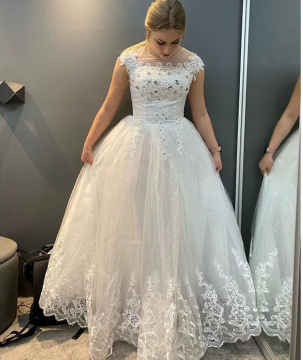 Woman wearing a white lace wedding dress in front of a mirror.