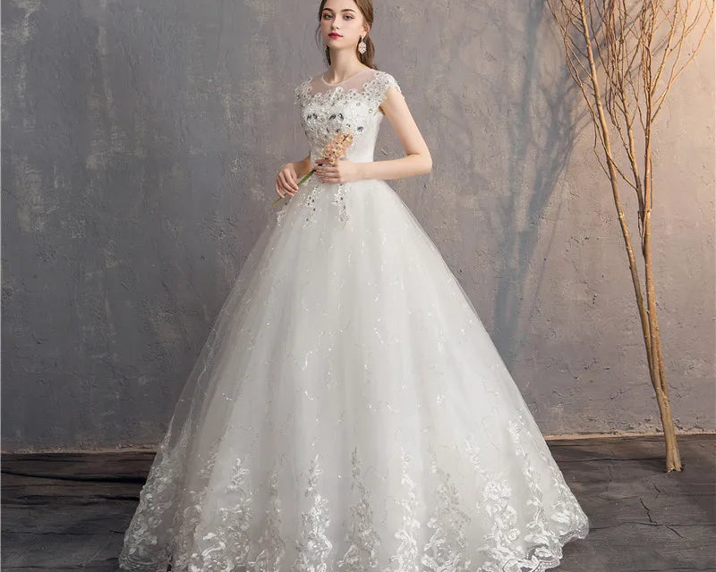 Woman in a white lace wedding dress holding flowers against a textured wall.