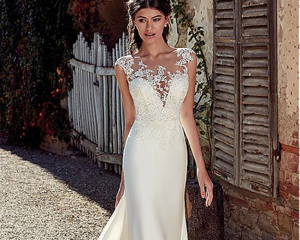 Woman in a white wedding dress standing outdoors near a rustic building.