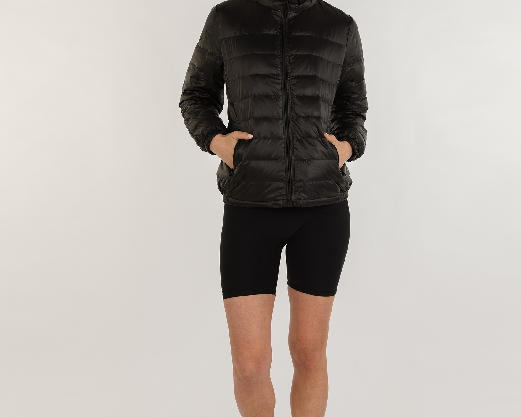 Person wearing a black puffer jacket and black shorts on a white background
