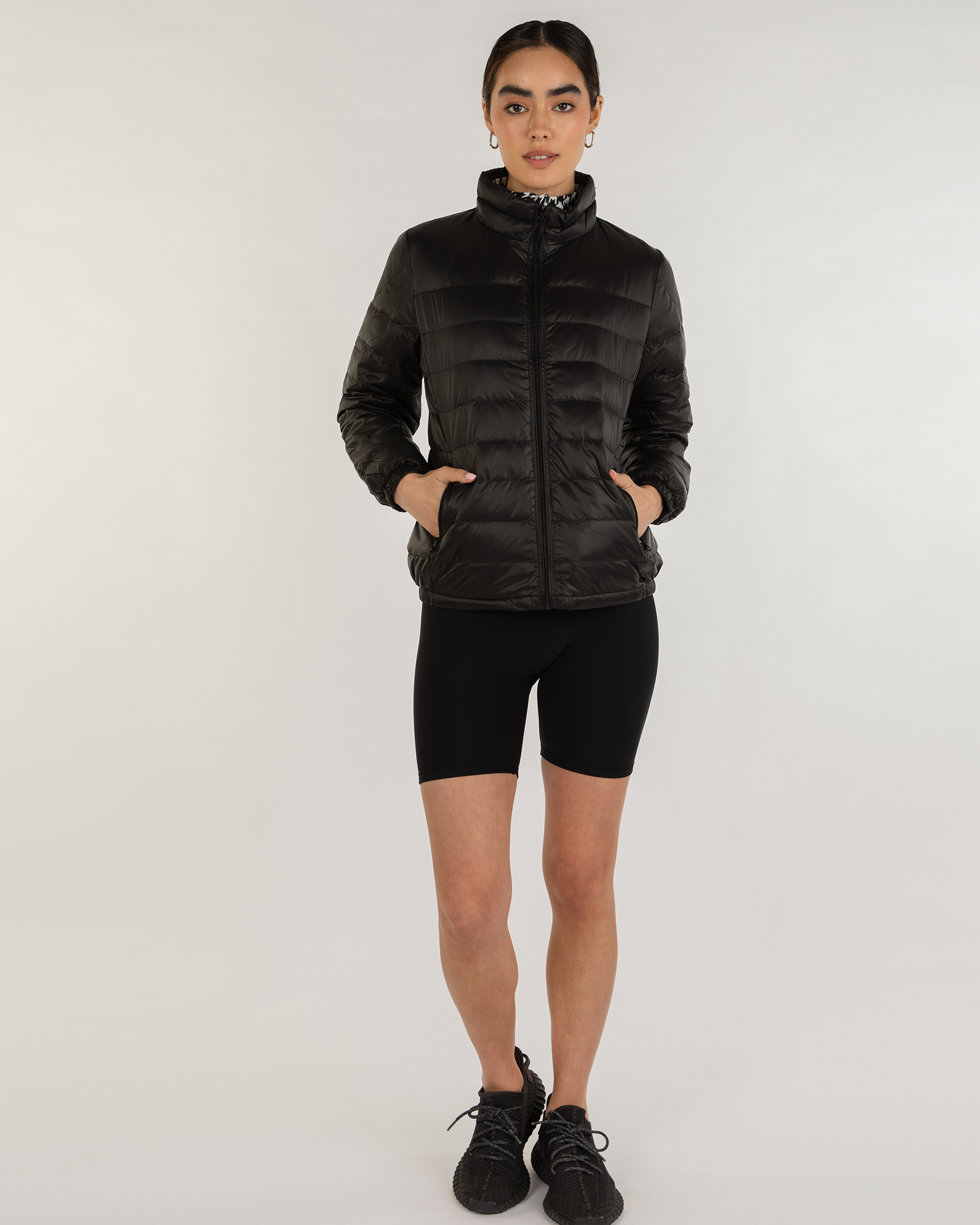 Person wearing a black puffer jacket and black shorts on a white background