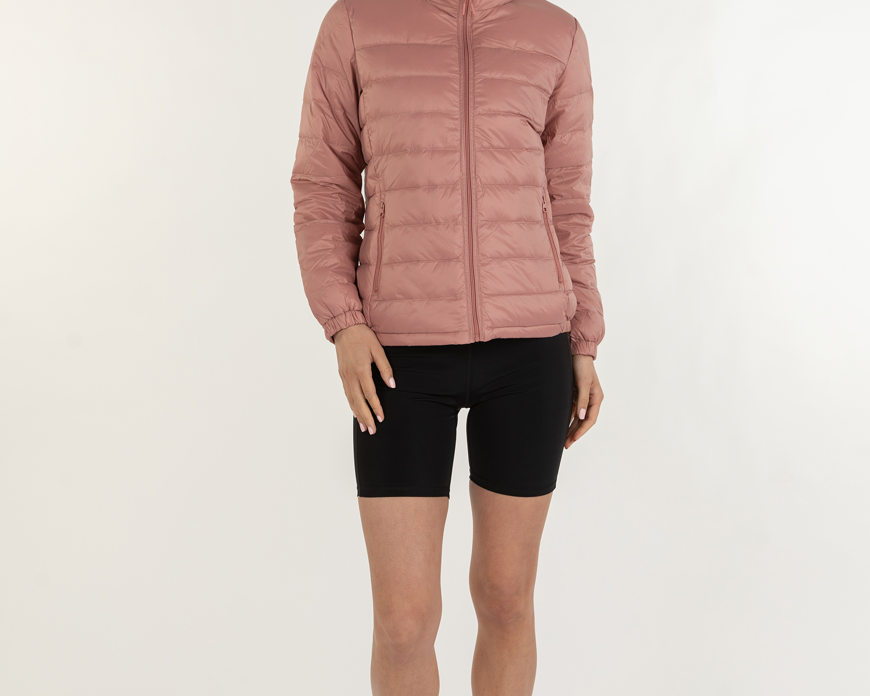 Person wearing a pink puffer jacket and black shorts on a white background