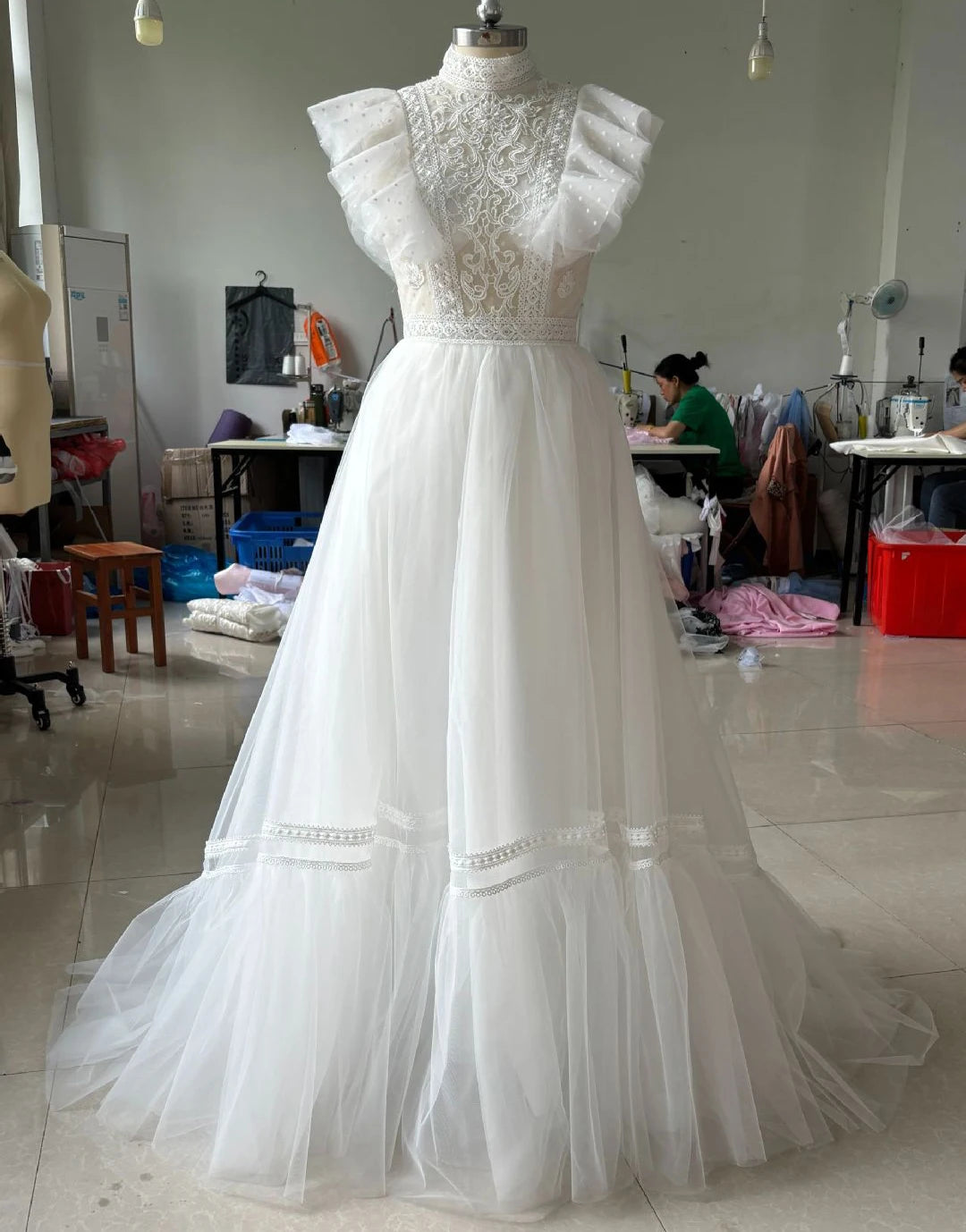 White lace wedding dress on a mannequin in a workshop setting.