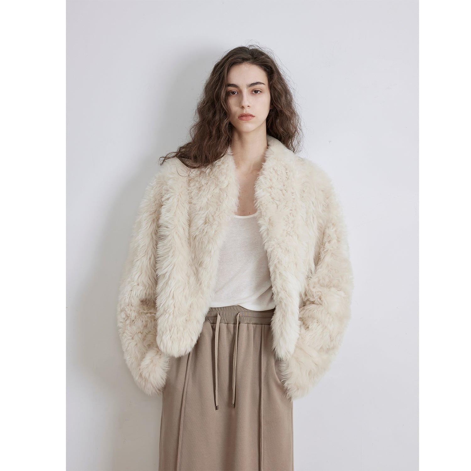 NEWYORKLISTED STYLE COLLECTION: Woman wearing a fluffy white jacket over a white shirt and beige pants on a light gray background