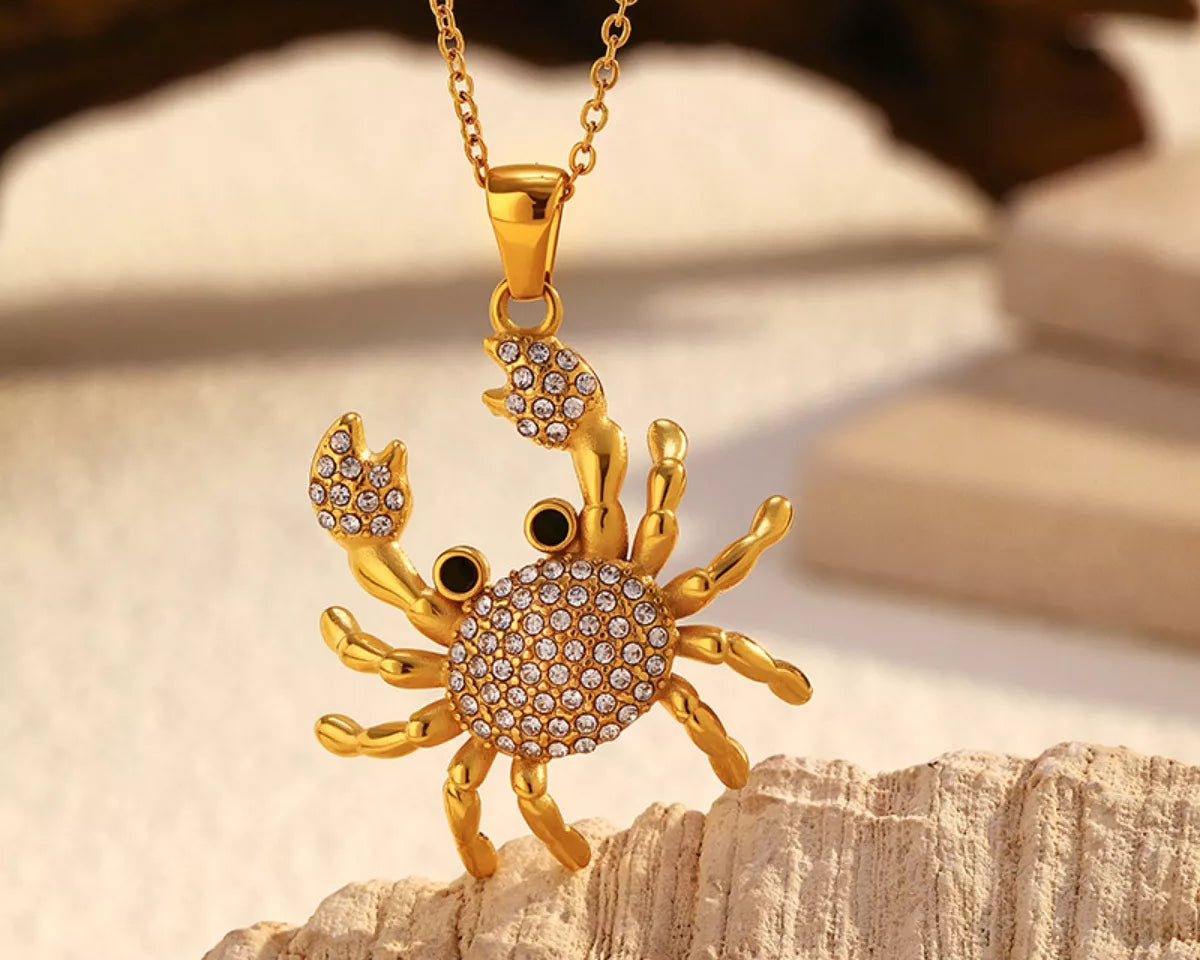 NYLD Glamour Collection by NEWYORKLISTED: Gold crab-shaped pendant necklace on a wooden surface