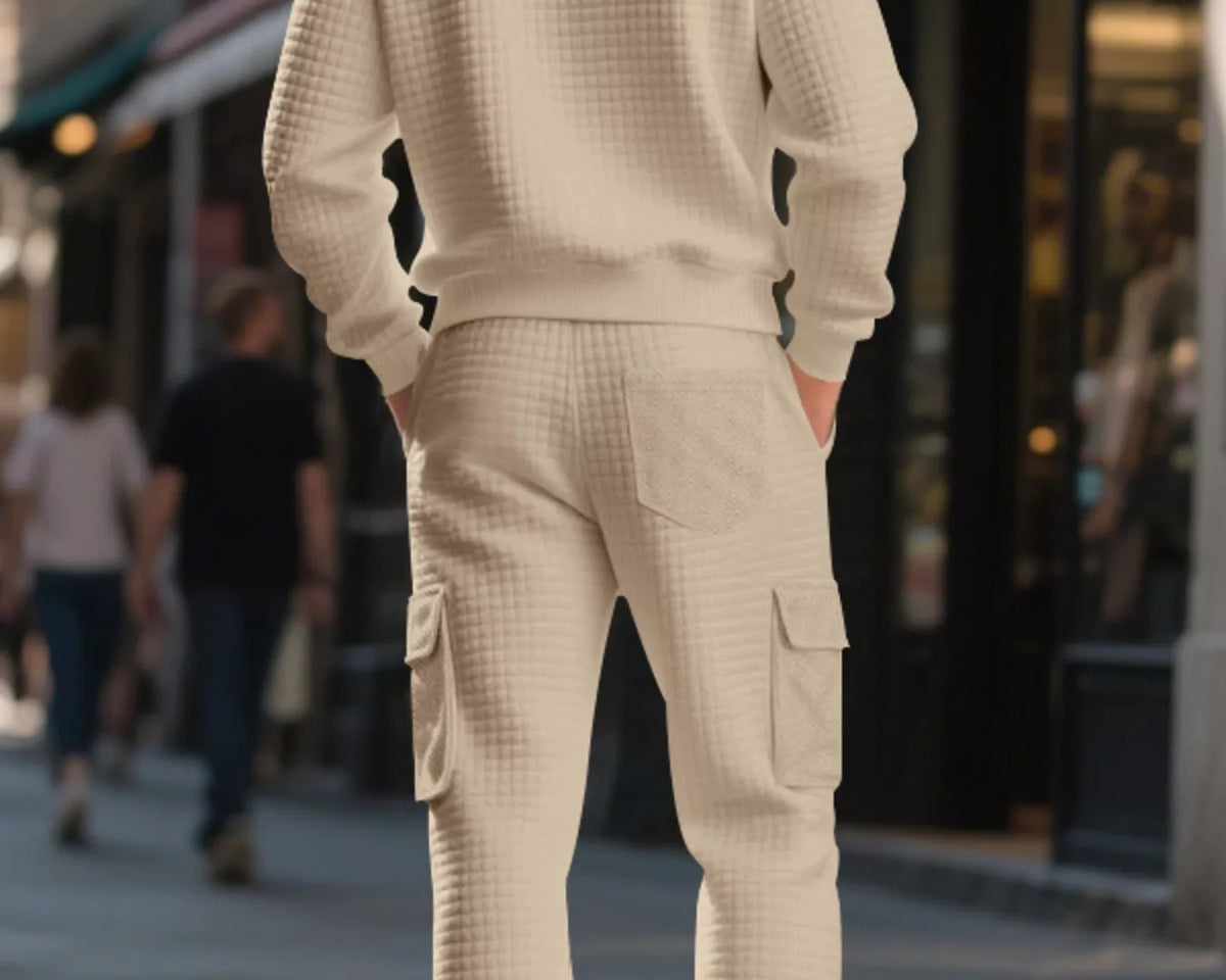 NEWYORKLISTED ATLAS MEN'S COLLECTION: A man viewed from behind wearing a cream-colored waffle-knit crewneck sweatshirt and matching cargo jogger pants on a city sidewalk.