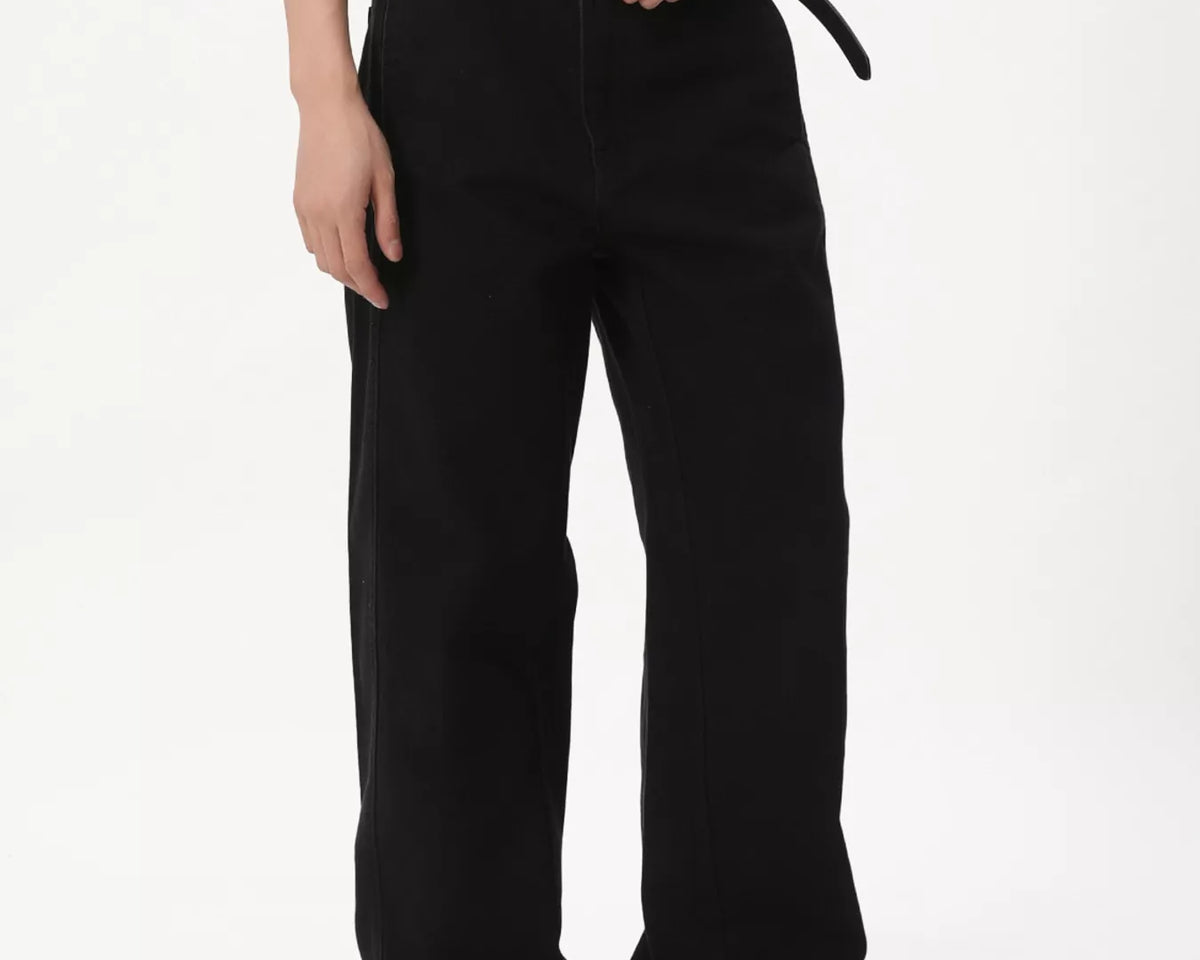 NEWYORKLISTED ATLAS MEN'S COLLECTION: A person wearing loose black wide-leg pants with a black belt, paired with a cream graphic T-shirt and black platform shoes, photographed against a plain white studio background.