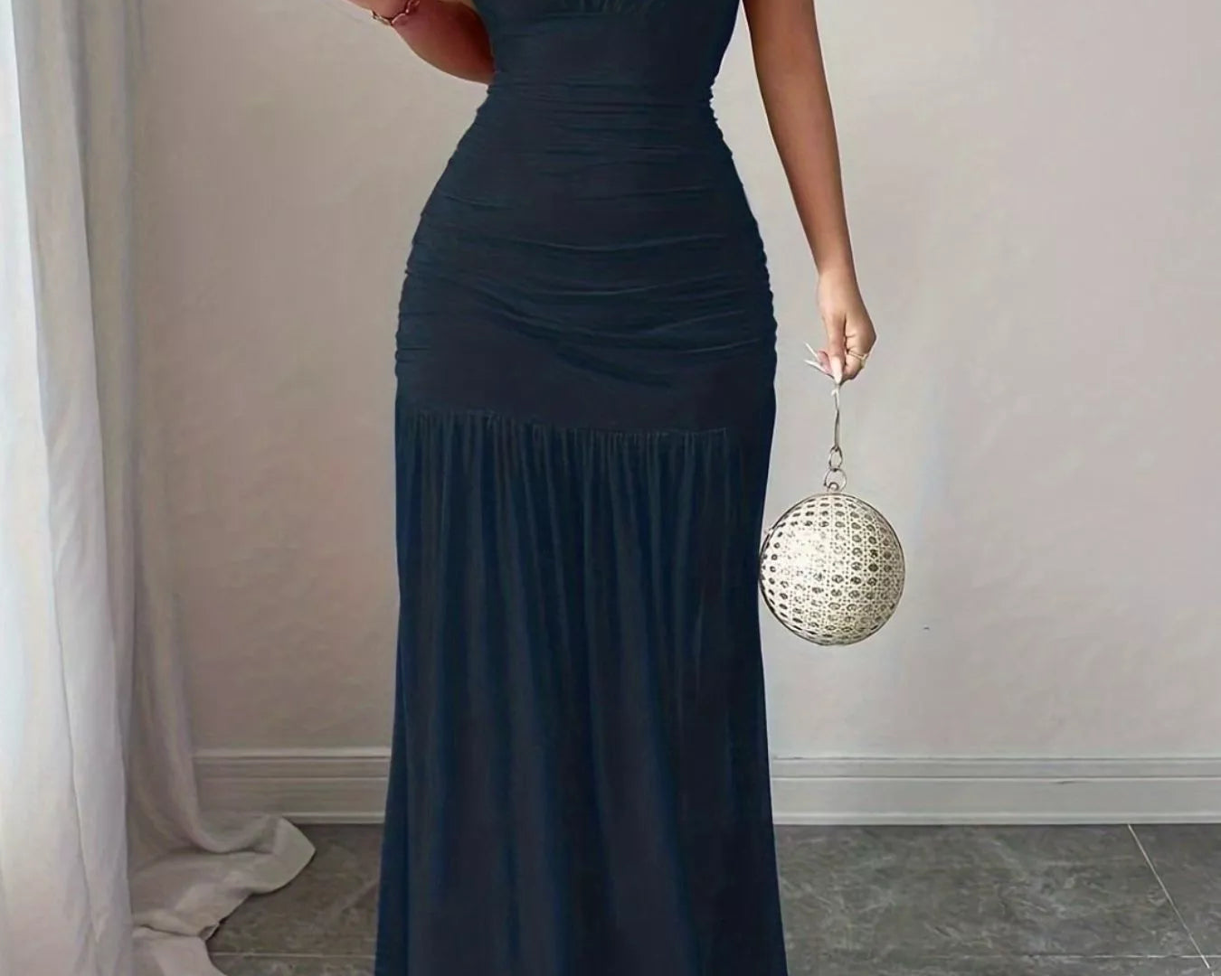 NEWYORKLISTED STYLE COLLECTION: Woman wearing a dark blue dress holding a disco ball in a room with light-colored walls and a gray floor.