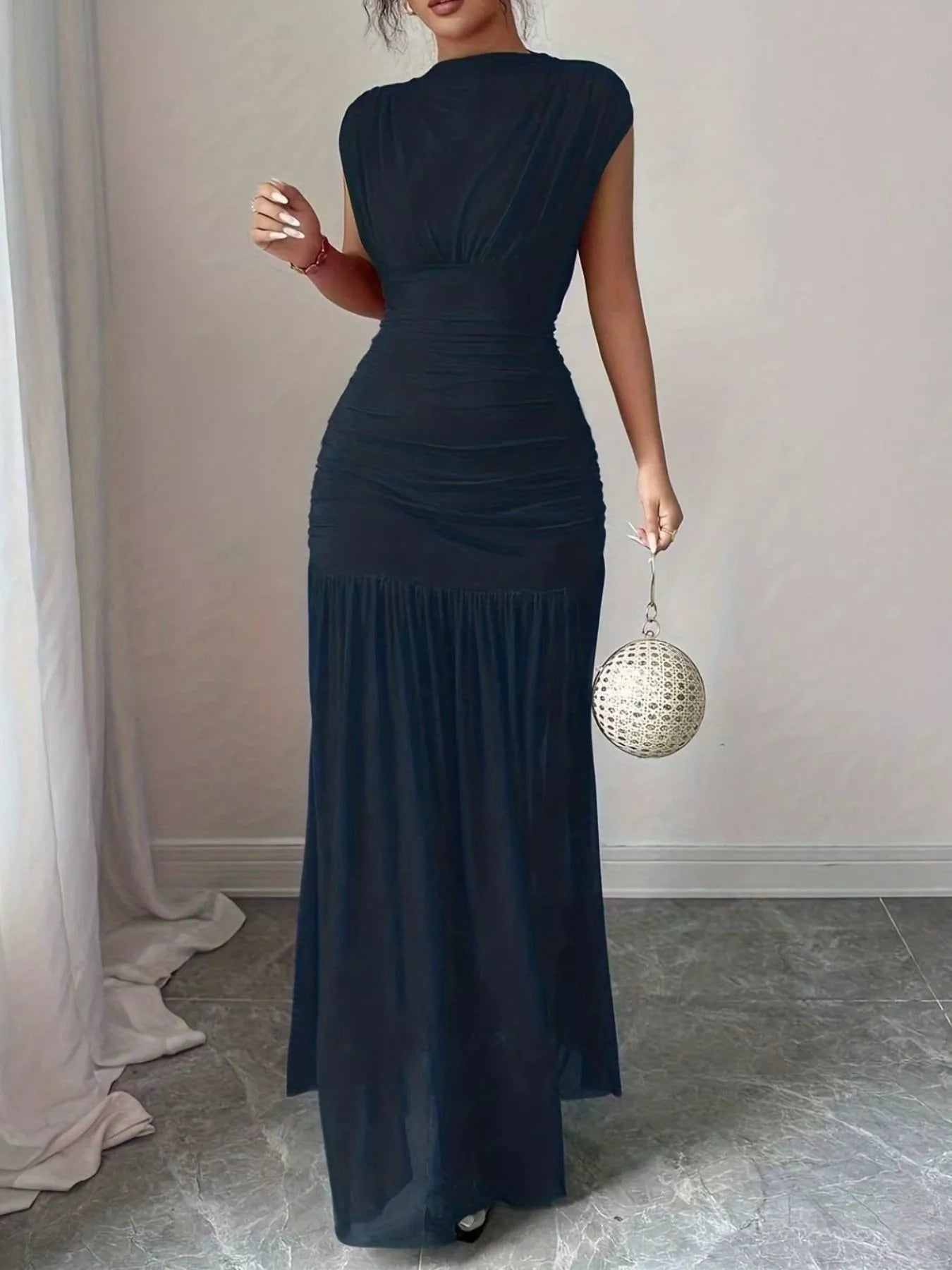 NEWYORKLISTED STYLE COLLECTION: Woman wearing a dark blue dress holding a disco ball in a room with light-colored walls and a gray floor.