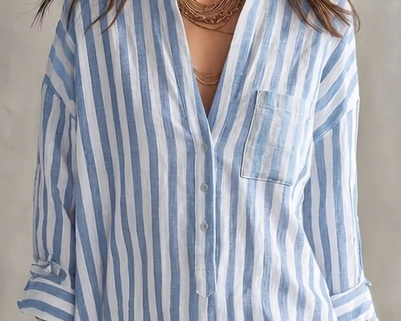 NEWYORKLISTED STYLE COLLECTION: A woman wearing a light blue and white vertically striped button-down shirt with a chest pocket, shown from the shoulders to the hips against a neutral studio background.