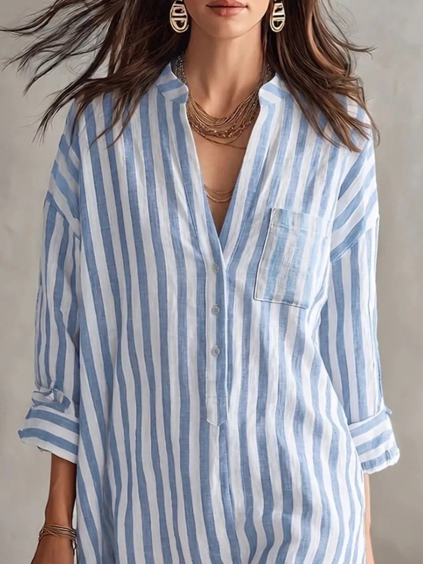 NEWYORKLISTED STYLE COLLECTION: A woman wearing a light blue and white vertically striped button-down shirt with a chest pocket, shown from the shoulders to the hips against a neutral studio background.