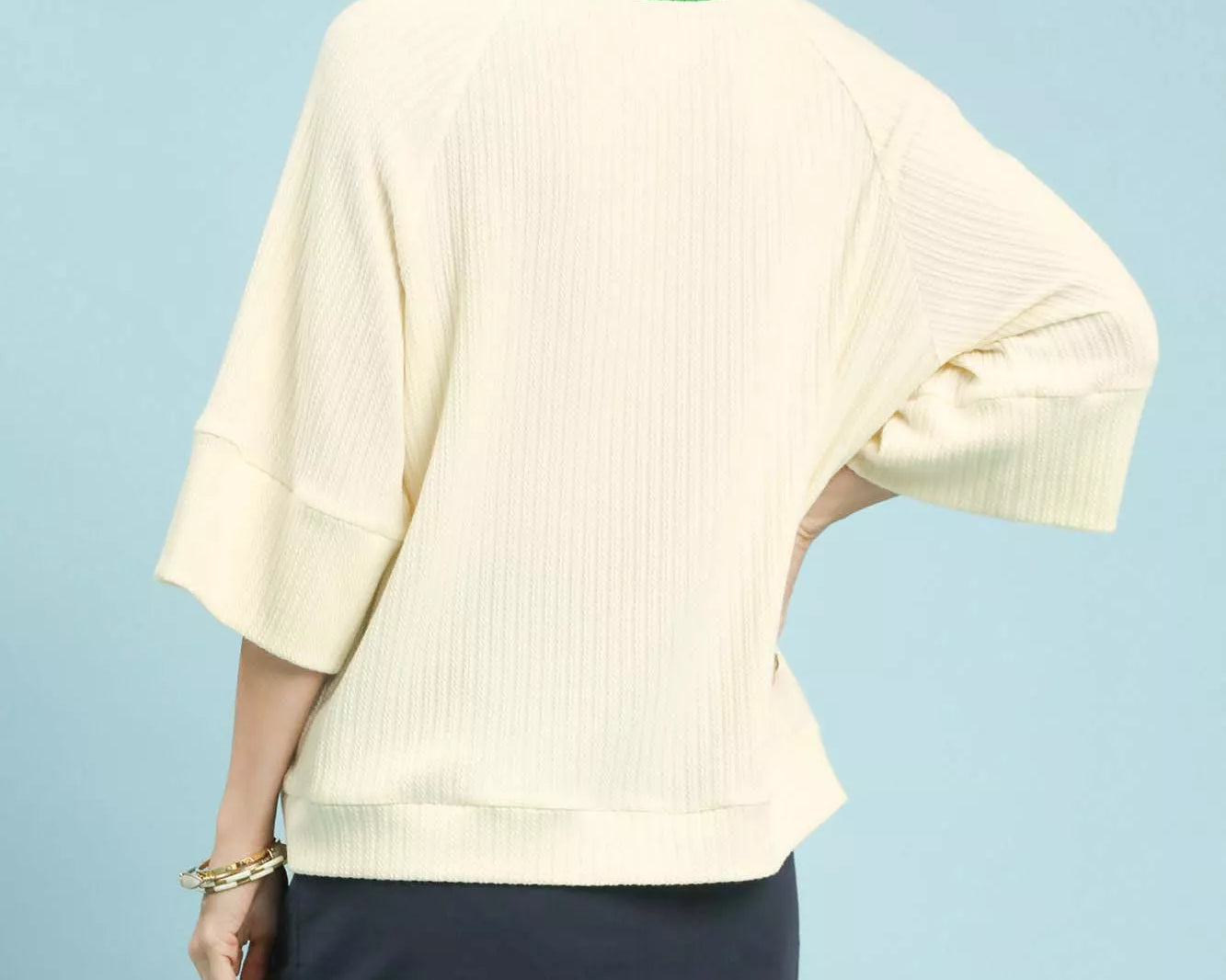 NEWYORKLISTED STYLE COLLECTION: Woman wearing a light-colored sweater and navy skirt on a light blue background