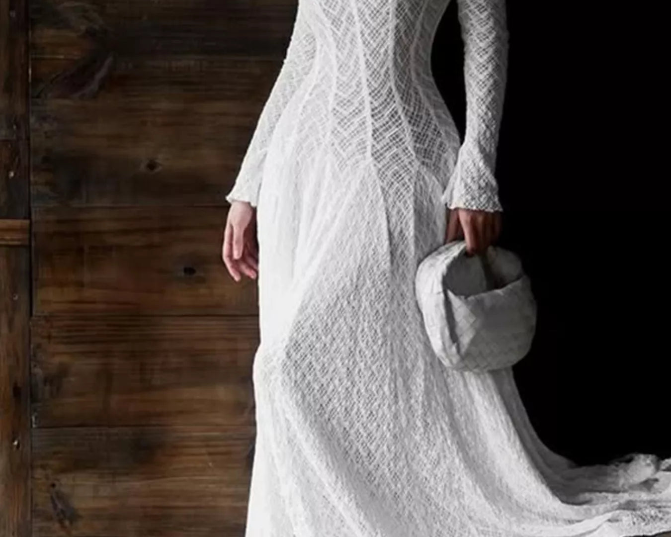 NEWYORKLISTED STYLE COLLECTION: Woman wearing a white lace dress holding a gray bag against a wooden background
