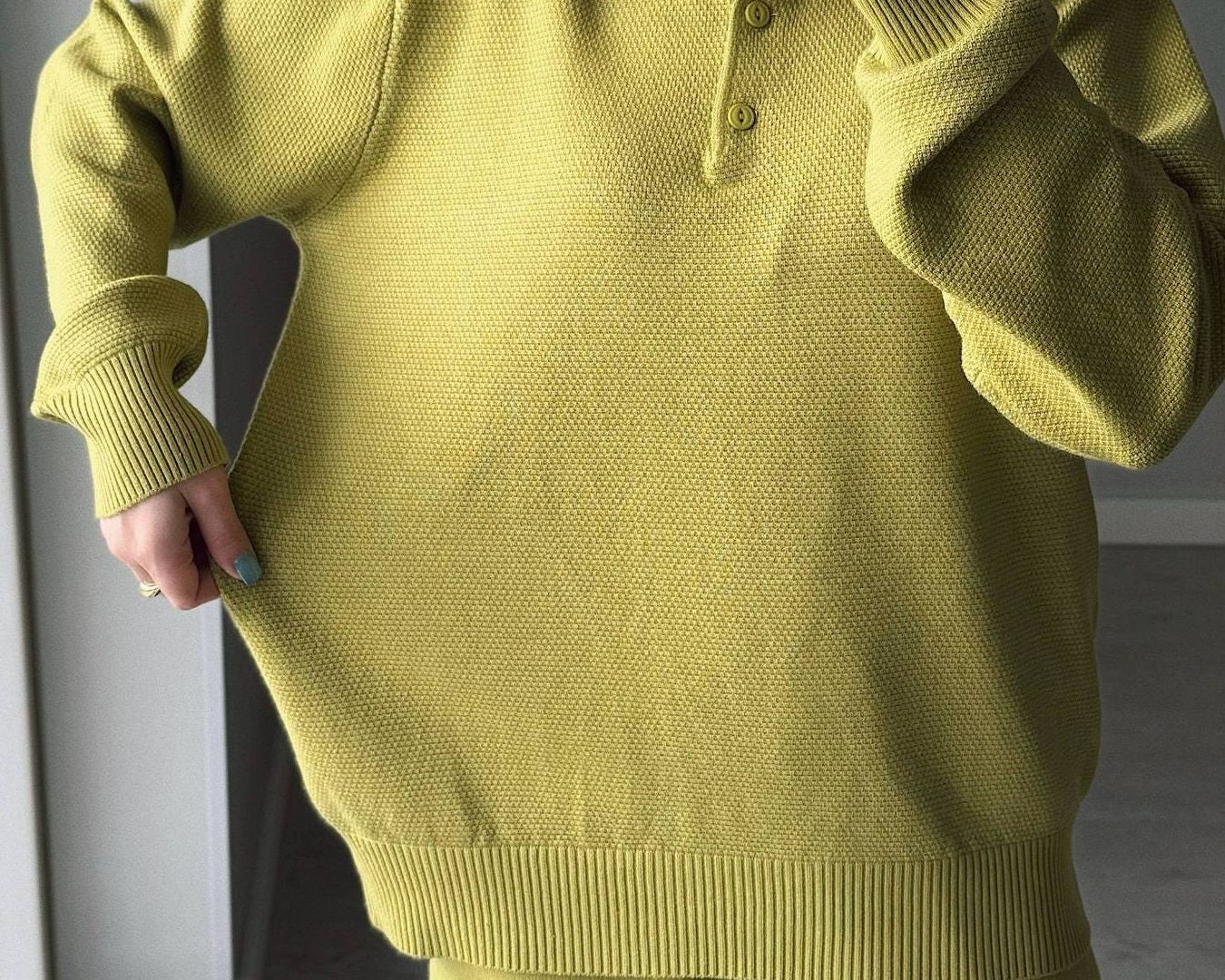 Person wearing a green sweater and pants taking a mirror selfie.