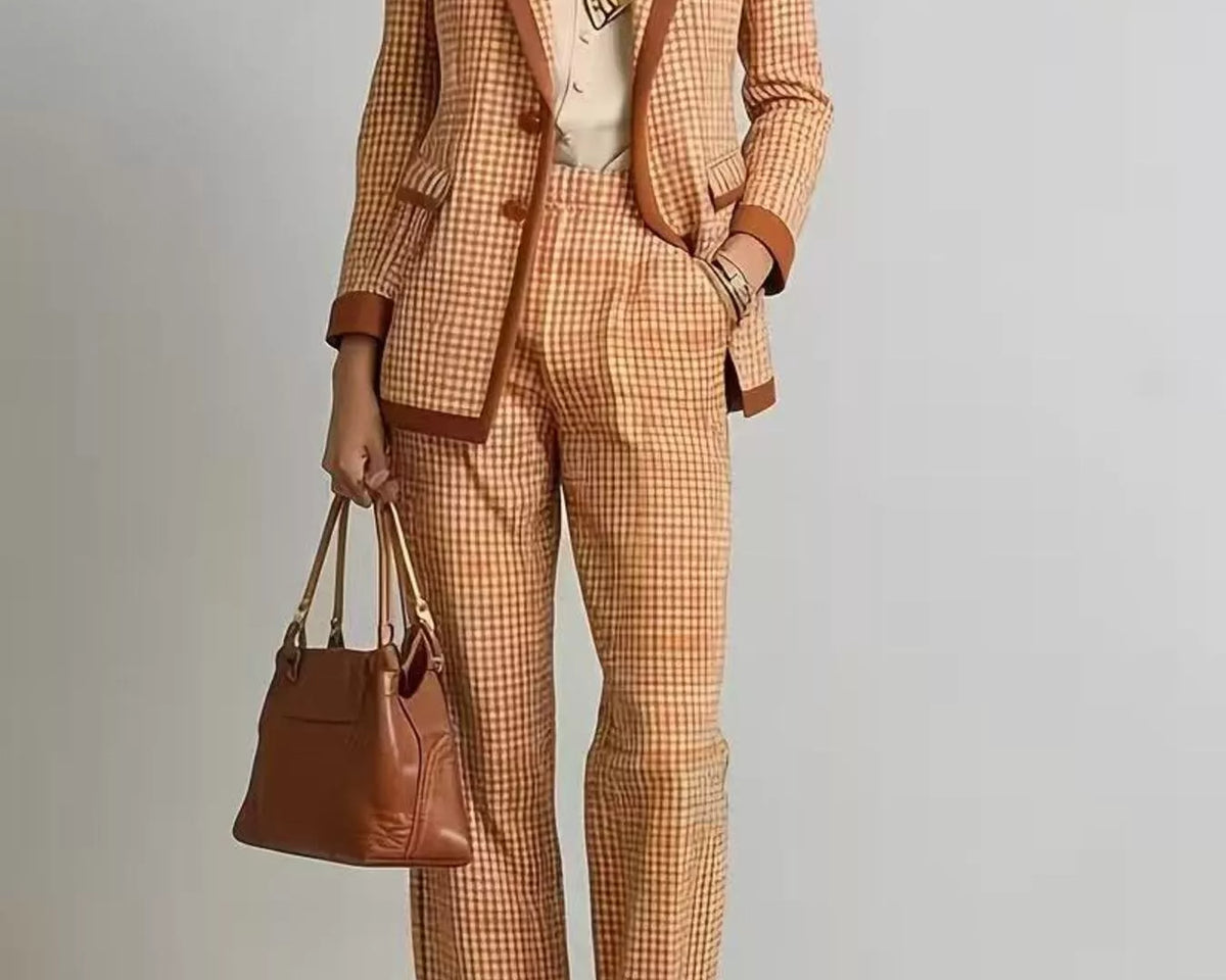 NEWYORKLISTED STYLE COLLECTION: A model wears a matching orange and beige checkered blazer and cropped trousers suit with brown leather trim, styled with a cream shirt, sunglasses, a brown leather handbag, and brown strappy heels against a light gray studio background.