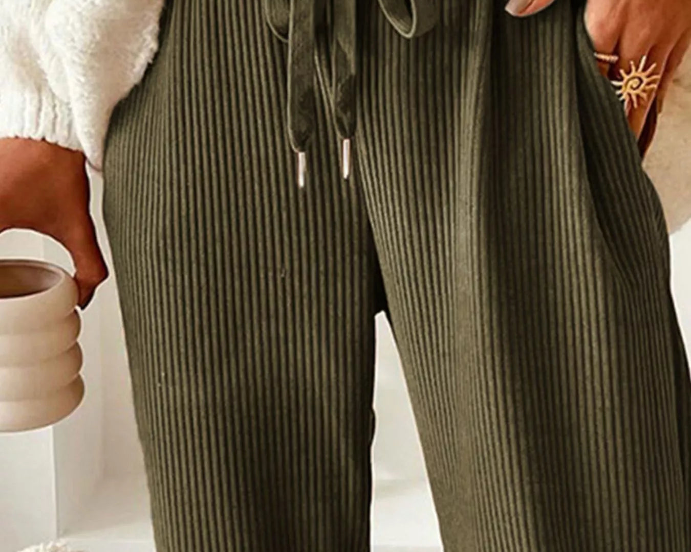 NEWYORKLISTED STYLE COLLECTION: Person wearing olive green ribbed pants with a white sweater and beige background