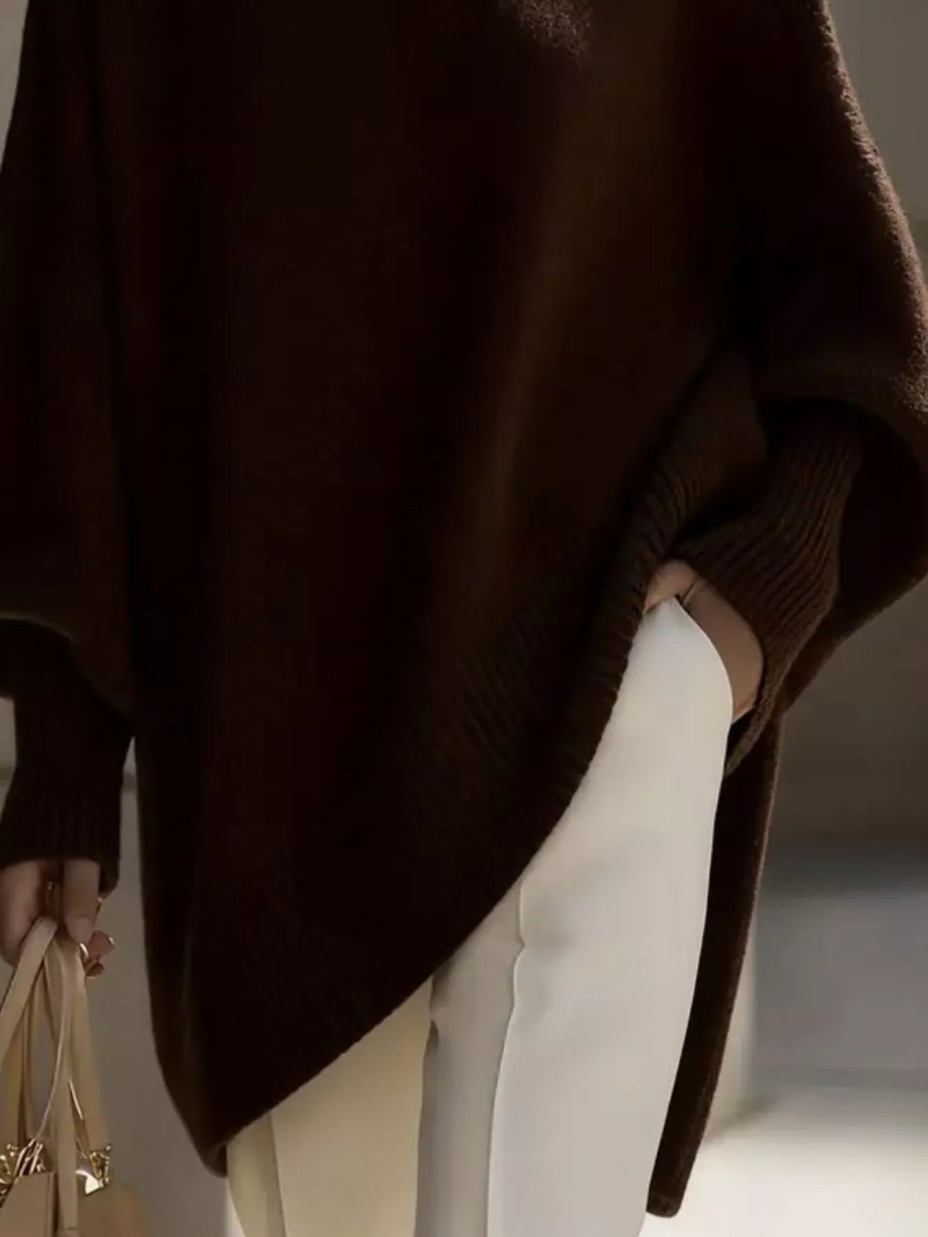 NEWYORKLISTED STYLE COLLECTION: Person wearing a brown poncho over a beige outfit, holding a beige handbag.