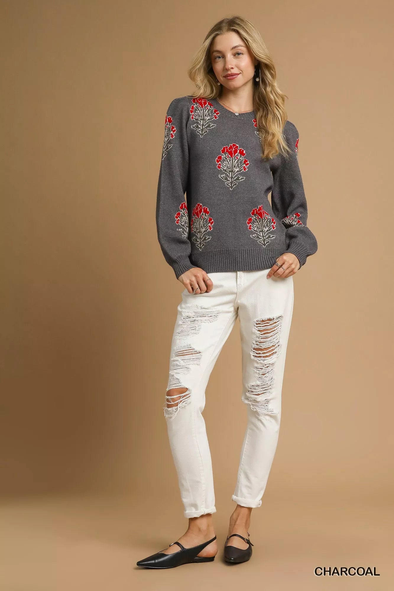 NEWYORKLISTED STYLE COLLECTION Woman wearing a charcoal gray sweater with floral patterns and white distressed jeans on a beige background.