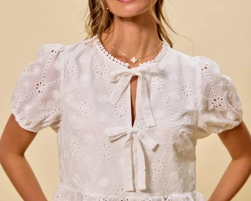 NEWYORKLISTED STYLE COLLECTION: Woman wearing a white embroidered blouse with puffed sleeves on a beige background