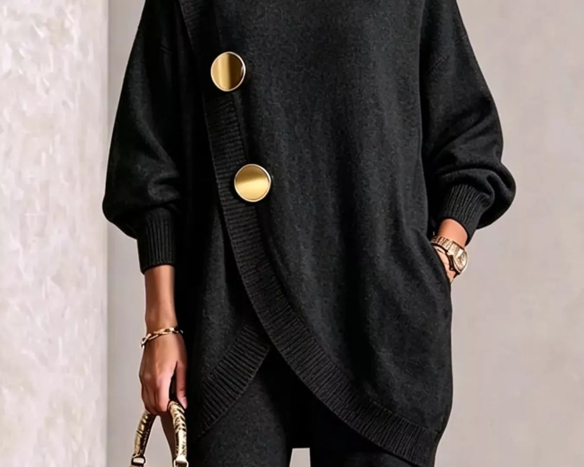 NEWYORKLISTED STYLE COLLECTION: A woman models a black oversized turtleneck sweater with asymmetrical gold buttons, paired with black pants and holding a small metallic gold handbag.