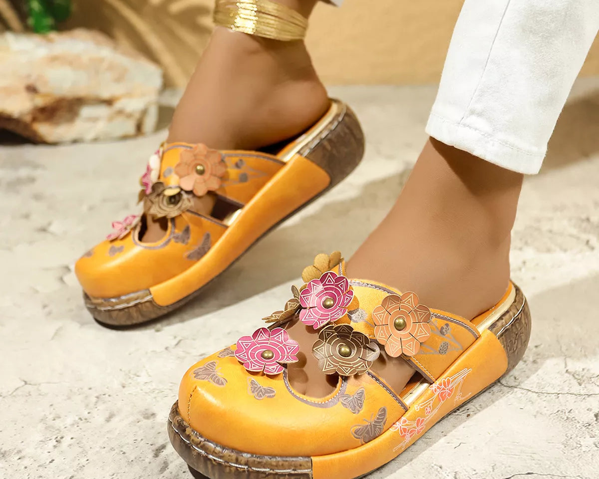 NEWYORKLISTED SHOE COLLECTION: Yellow sandals with floral designs worn by a person on a stone surface.