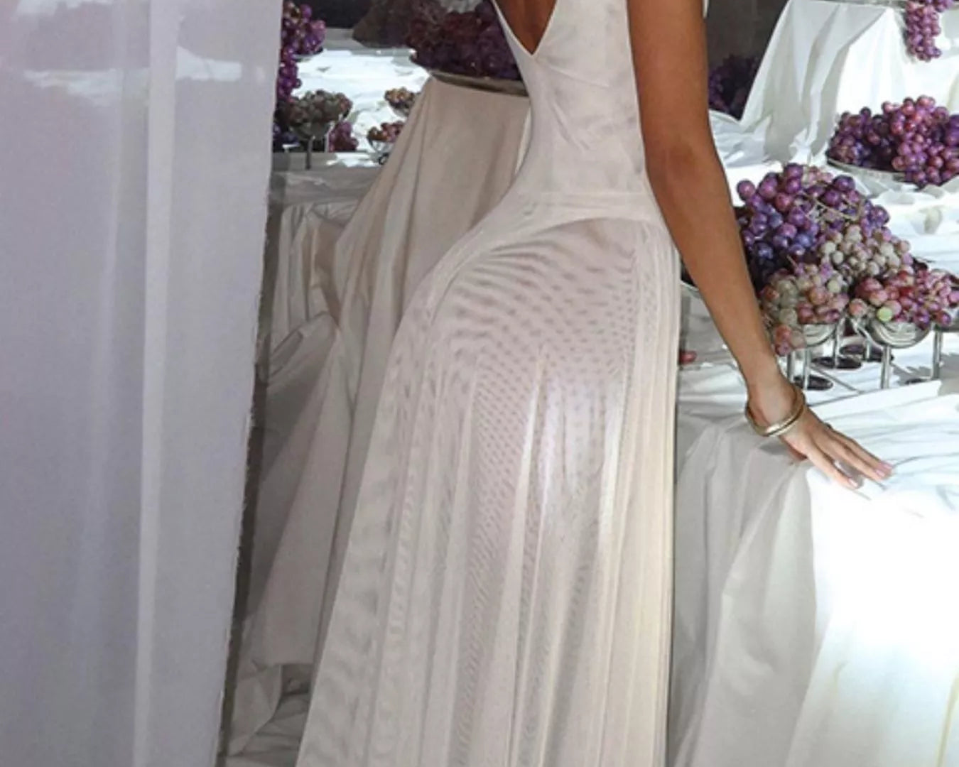 NEWYORKLISTED STYLE COLLECTION: Woman in a white dress standing in front of a decorated table with purple flowers.