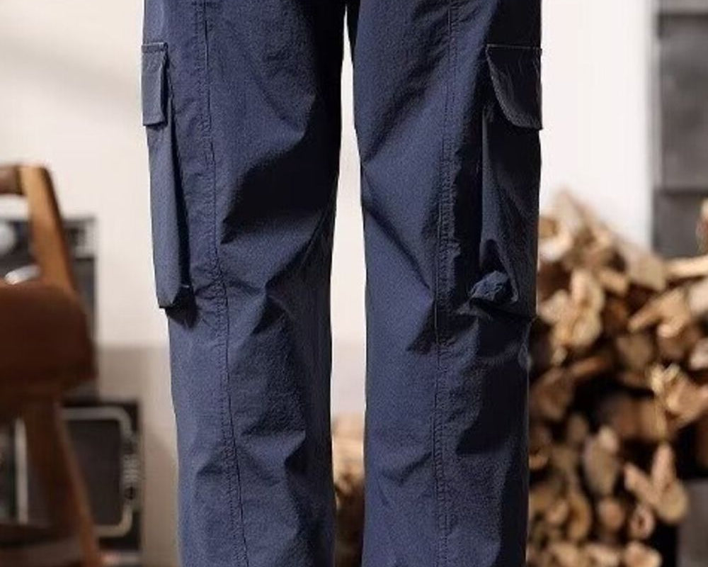 NEWYORKLISTED ATLAS MEN's COLLECTION: Person wearing navy cargo pants in an indoor setting with wooden logs in the background