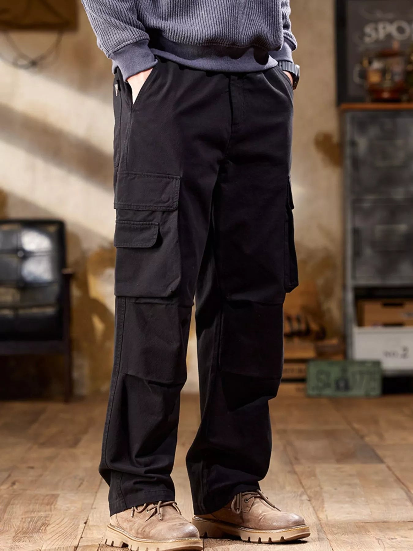 NEWYORKLISTED ATALS MEN's COLLECTION: Person wearing dark cargo pants with multiple pockets in an indoor setting.