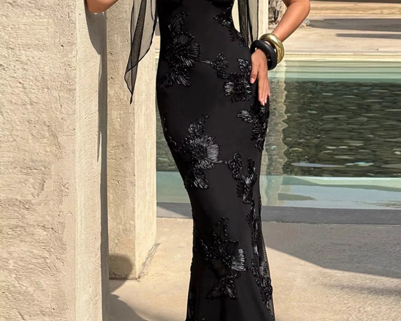 NEWYORKLISTED STYLE COLLECTION: Woman in a black lace evening gown standing by a stone wall.