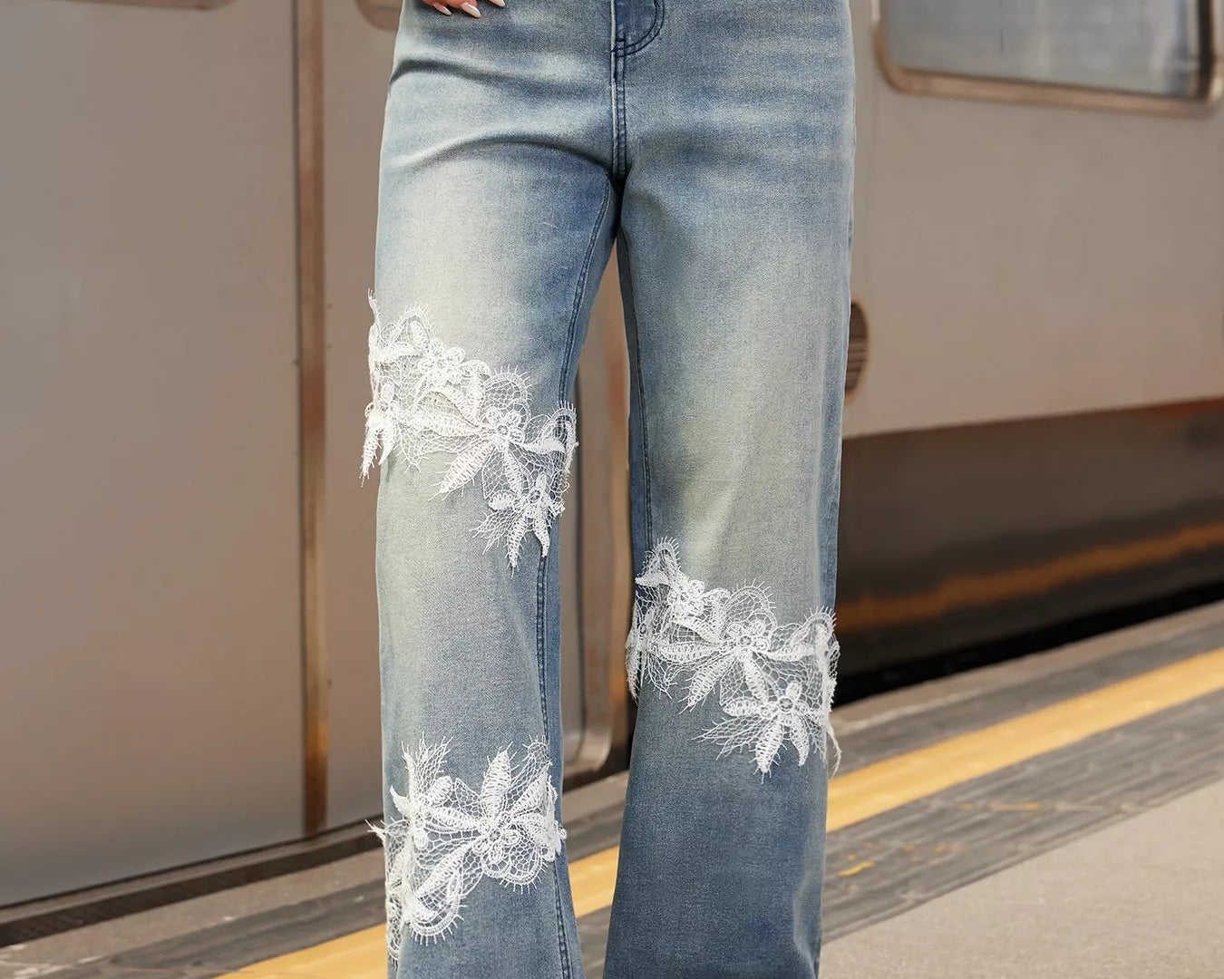 NEWYORKLISTED STYLE COLLECTION: Person wearing blue jeans with floral embroidery on a train platform.