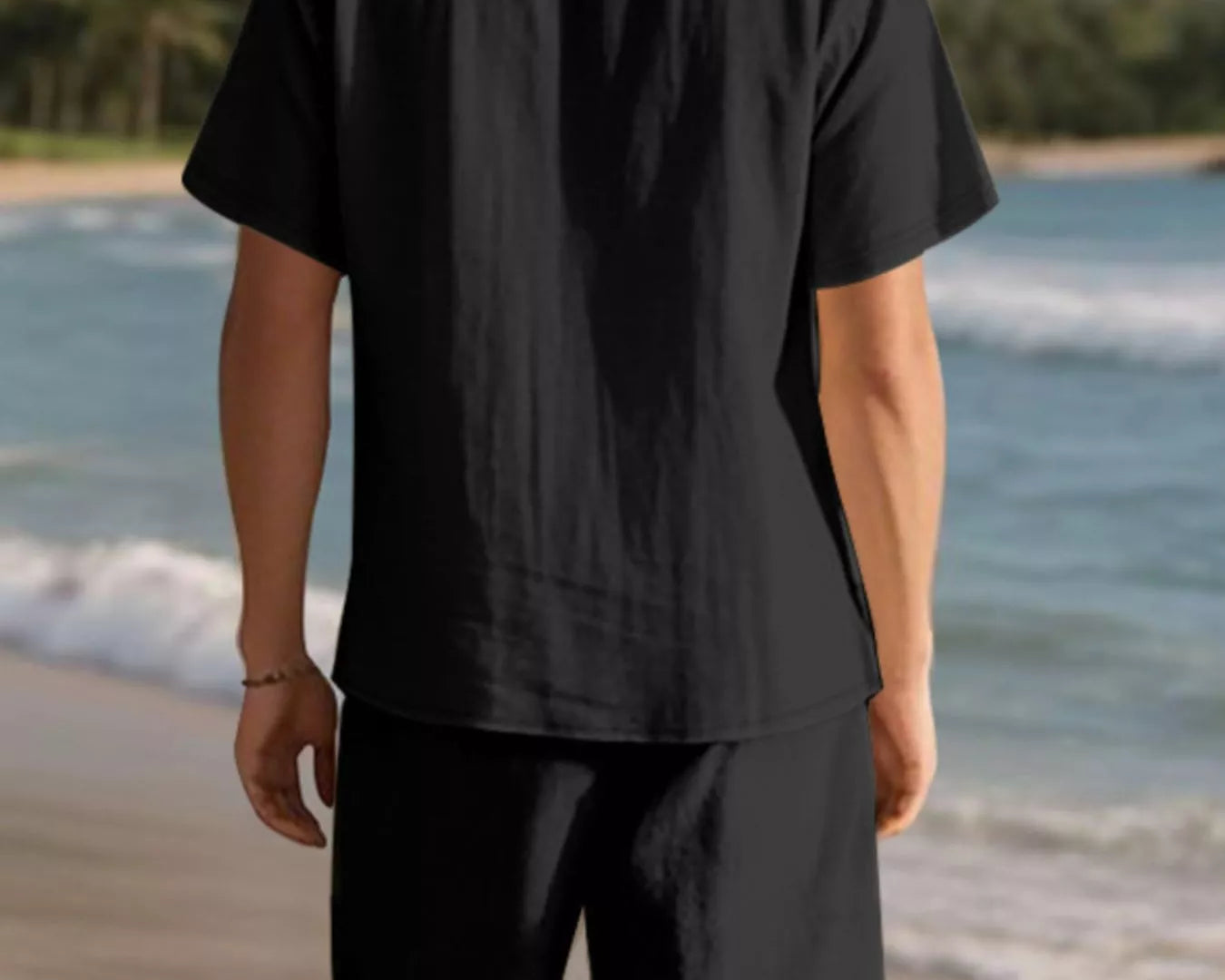 NEWYORKLISTED ATLAS MEN'S COLLECTION: Person wearing a black shirt and shorts standing on a beach with mountains in the background