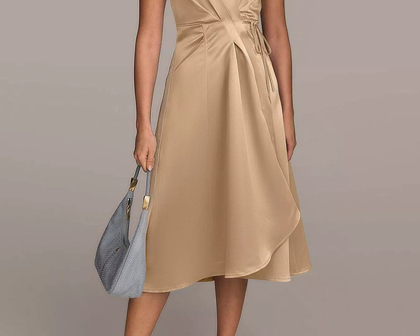 NEWYORKLISTED RUNWAY STYLE: Woman wearing a beige dress holding a blue handbag on a plain background
