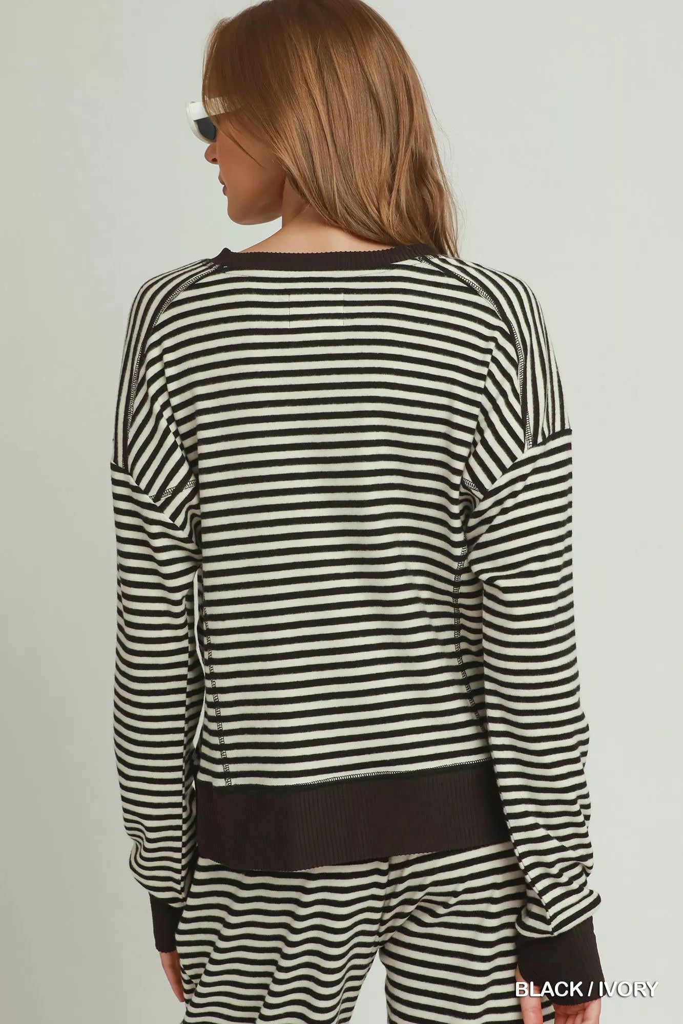 NEWYORKLISTED COMFORT COLLECTION: A woman shown from the back wearing a black and off-white horizontally striped long-sleeve top and matching striped pants against a plain light background.