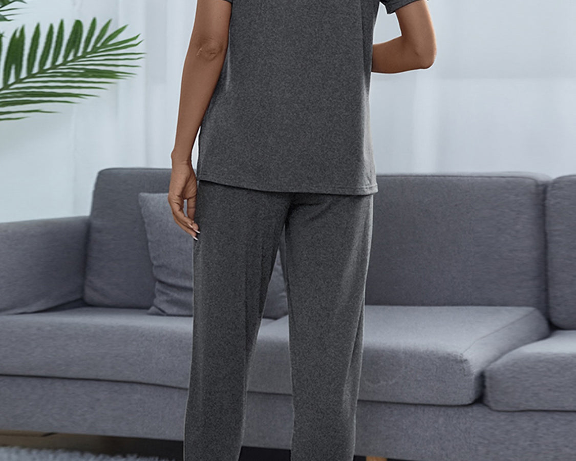NEWYORKLISTED Intimate Apparel: Person wearing a gray pajama set standing in a living room with a gray sofa and white walls.