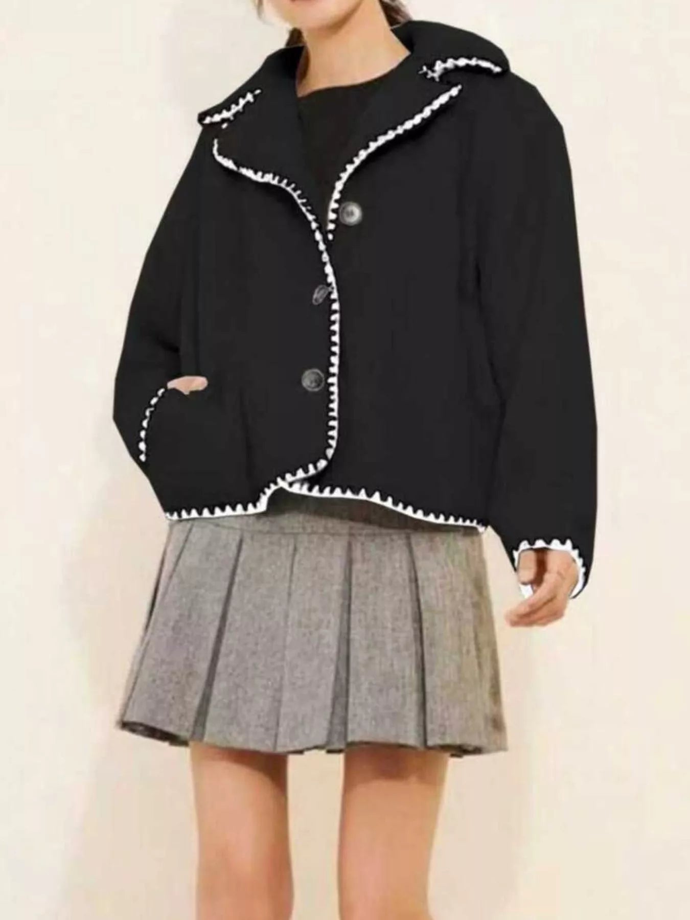 NEWYORKLISTED STYLE COLLECTION: Black jacket with white trim worn over a gray pleated skirt on a plain background