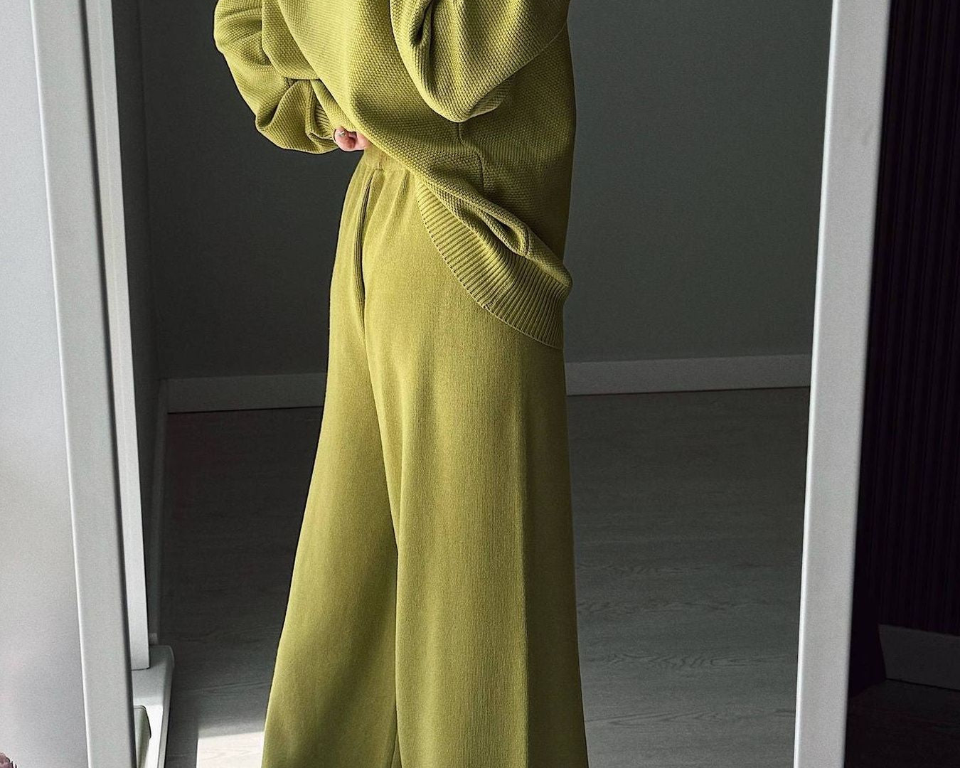 Person wearing a green knit outfit standing in front of a mirror.
