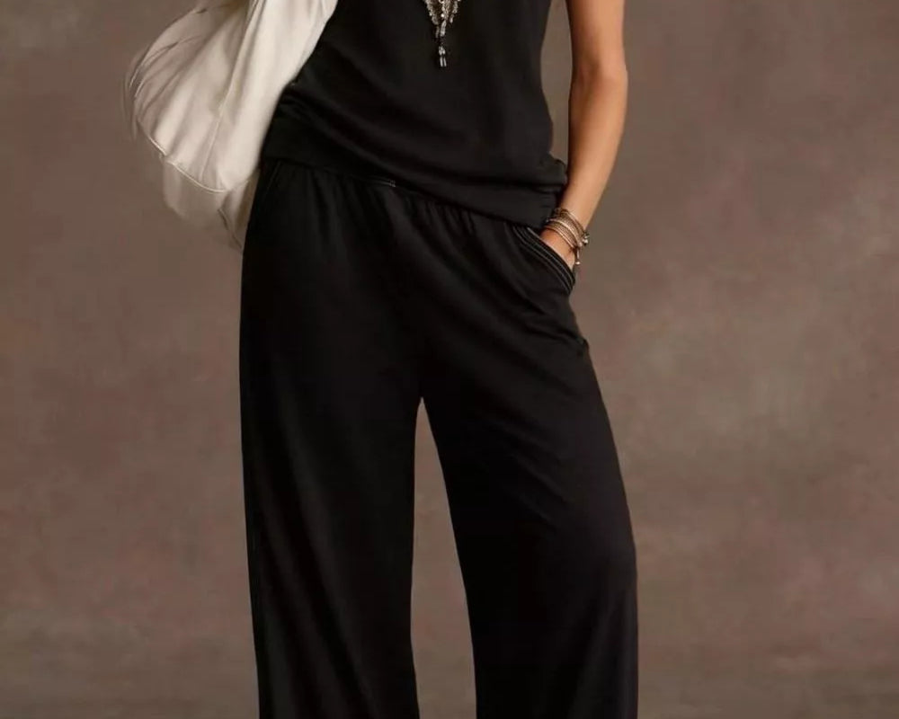 NEWYORKLISTED STYLE COLLECTION: Woman wearing a black jumpsuit with a white bag against a brown background
