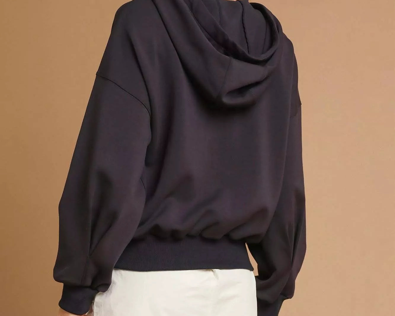 NEWYORKLISTED STYLE COLLECTION: Person wearing a dark hoodie and white shorts with a beige cap on a brown background