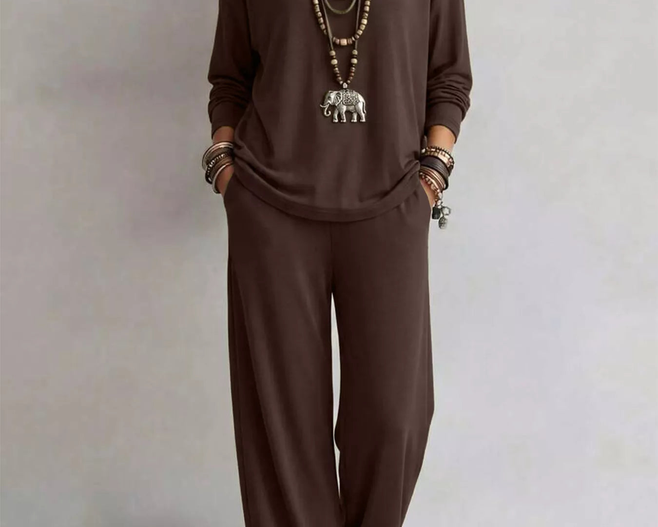 NEWYORKLISTED STYLE COLLECTION: A woman modeling a dark brown long-sleeve top and matching wide-leg pants set, accessorized with layered necklaces, bracelets, and sandals, against a neutral studio background.