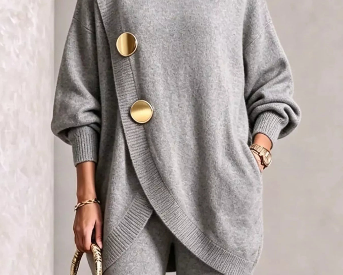 NEWYORKLISTED STYLE COLLECTION: A woman wearing a light gray knit turtleneck sweater with oversized gold buttons and matching gray knit pants, holding a small gold handbag against a neutral indoor background.