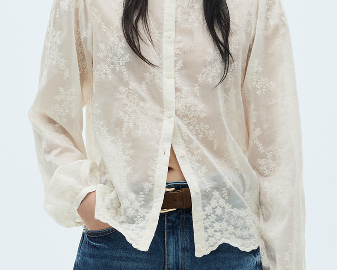 NEWYORKLISTED STYLE COLLECTION: Person wearing a sheer white lace blouse over a black top with blue jeans on a light gray background