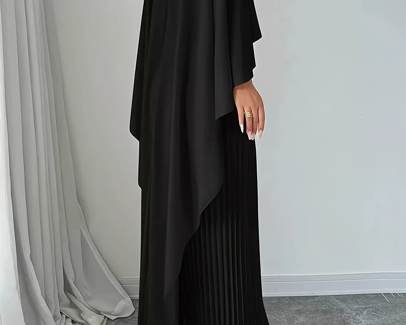 NEWYORKLISTED STYLE COLLECTION: Black pleated dress worn by a person against a white wall.