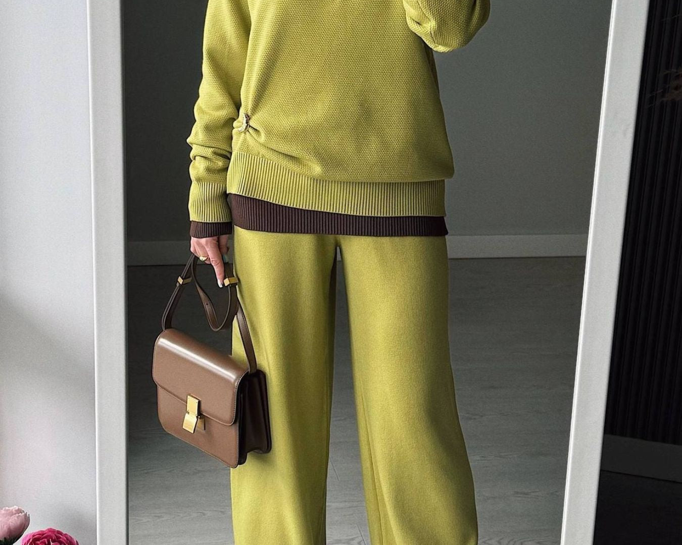 NEWYORKLISTED Comfort Collection: Person wearing a green sweater and pants holding a brown handbag, standing in front of a mirror.