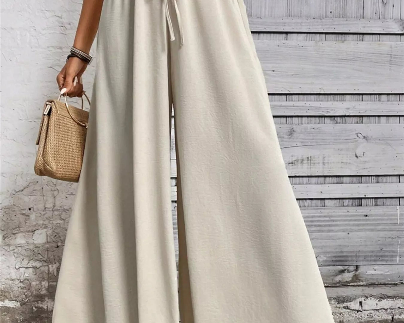 NEWYORKLISTED STYLE COLLECTION: Person wearing beige wide-leg pants with a white top against a wooden wall.