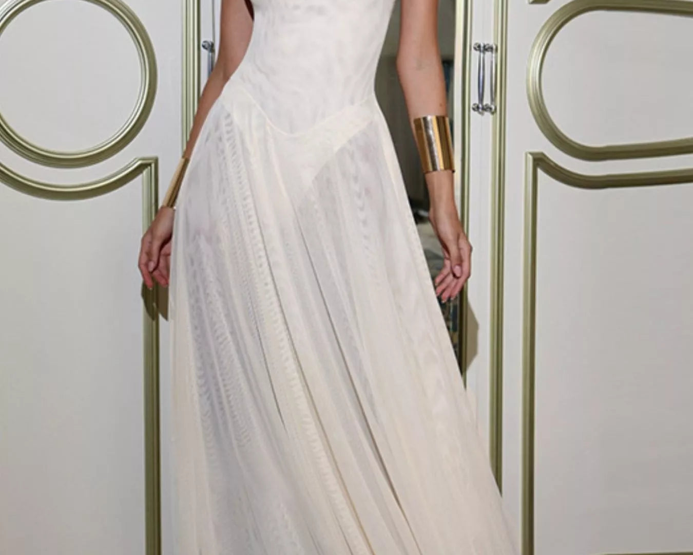 NEWYORKLISTED STYLE COLLECTION: Woman wearing a white dress with gold arm bands in an elegant interior setting.