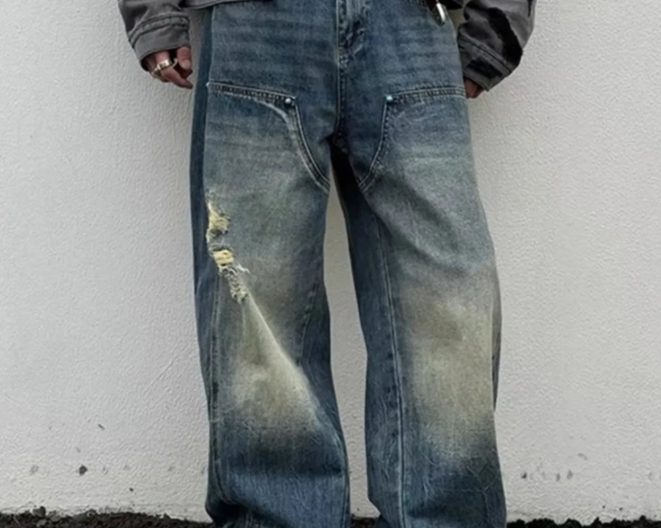 NEWYORKLISTED ATLAS MEN's COLLECTION: Person wearing distressed blue jeans and a dark jacket against a white wall.