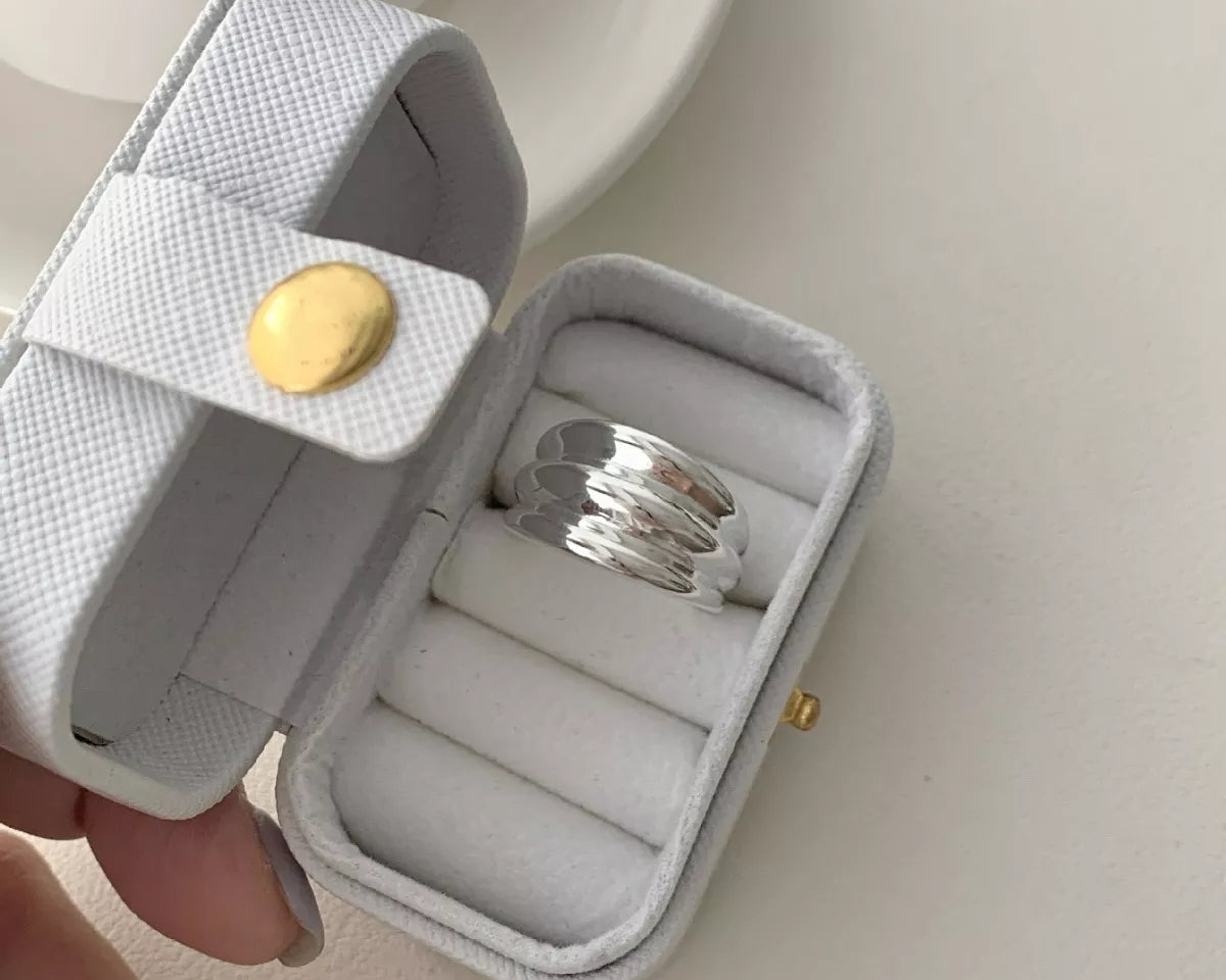 NYLD Glamour Collection: Silver ring in a white jewelry case with a gold button on a light background