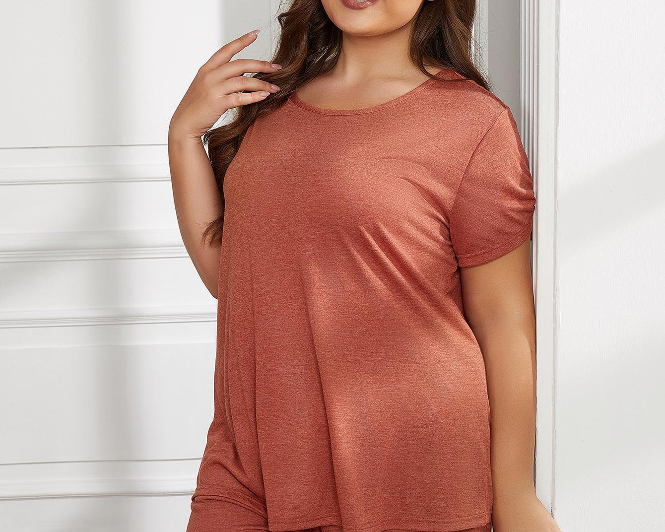 NEWYORKLISTED Intimate Apparel Collection: Woman wearing a rust-colored outfit standing against a white wall.