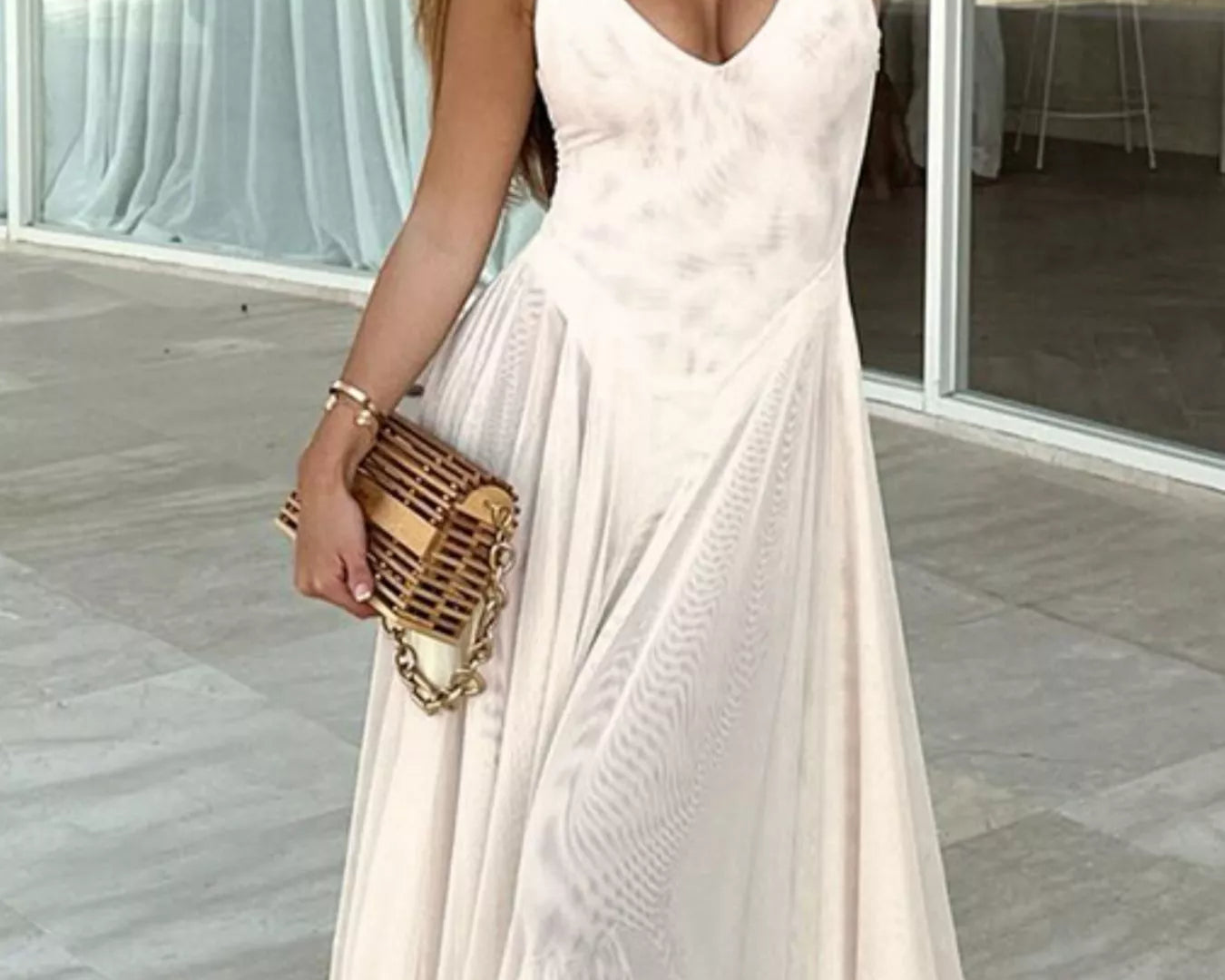 NEWYORKLISTED STYLE COLLECTION: Woman in a white dress holding a gold clutch in an indoor setting.